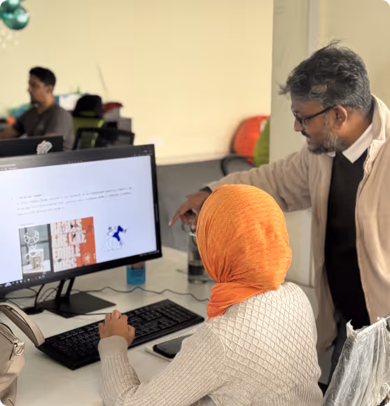 Two people reviewing work together at a desktop computer in the office.